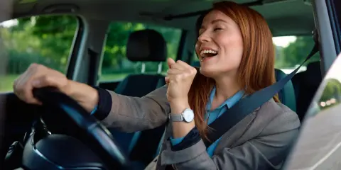 Mujer sonríe y canta al volante, feliz de conducir en España con su carnet de conducir ucraniano.