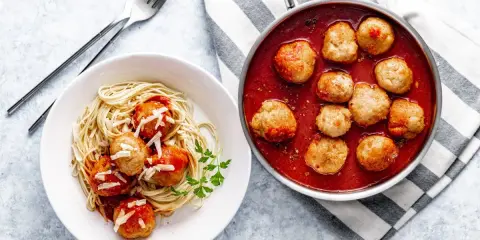 Pyszne pulpety w sosie pomidorowym z makaronem spaghetti, posypane parmezanem. Obok patelnia z gorącymi pulpetami w sosie.