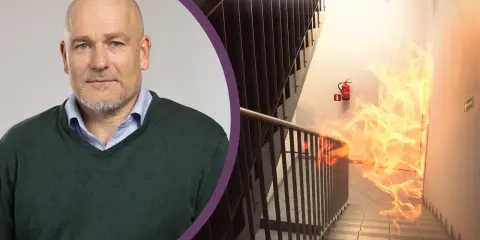 Man med skägg och en brandhärjad trappa med brandsläckare. Viktigt med revisionsbesiktning brandlarm för säkerheten.