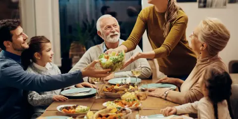 Une famille partage un repas joyeux. La mère sert la salade, et tout le monde sourit. C'est un moment de partage, alors pourquoi ne pas mettre les coudes sur la table ?