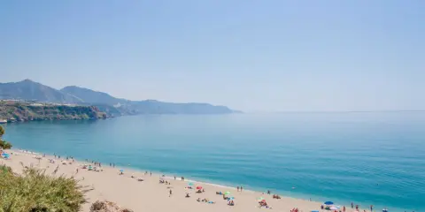 Sonniger malaga strand mit vielen Menschen, die sich unter bunten Sonnenschirmen entspannen. Das türkisfarbene Meer lädt zum Baden ein.