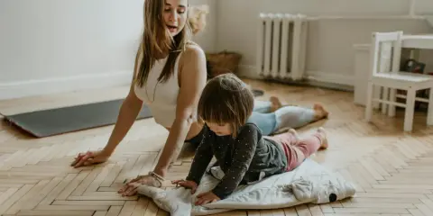 Mama uczy dziecko nauki oddychania podczas ćwiczeń jogi. Dziecko leży na poduszce w kształcie rekina, a mama w pozycji kobry.