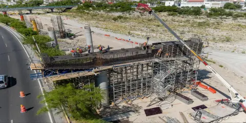 Obreros trabajan en la construcción de puentes de acero, con grúas y andamios rodeando las estructuras.