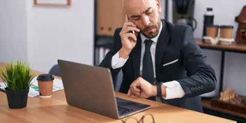 Zmęczony biznesmen sprawdza zegarek, zastanawiając się nad wymiarem czasu pracy.