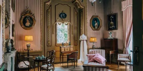 Eleganckie wnętrze pałacu w Nieborowie. W pokoju z różowo-białymi pasami na ścianach, zabytkowe meble, obrazy i manekin w sukni.