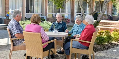 Anziani riuniti in giardino, chiacchierano e sorridono. Un momento sereno nella loro casa di riposo RSA.