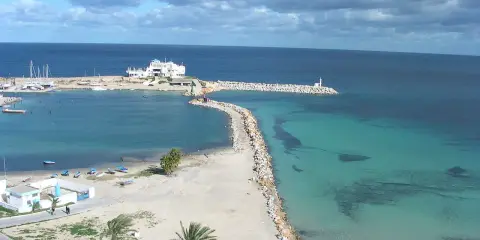 Piękna plaża i turkusowe morze w Tunezji. Październikowa pogoda sprzyja spacerom brzegiem, gdzie widać białe budynki i palmy.