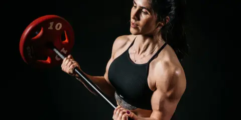 Frau mit starker Muskulatur hebt eine Langhantel. Ein effektiver Trainingsplan für Frauen.