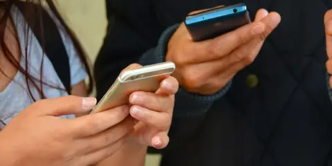 Zwei Hände halten Smartphones. Eine Frau hält ein goldenes iPhone, ein Mann ein blaues Handy. Vielleicht kommen eingehende Anrufe nicht an.