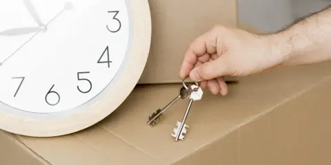 Un reloj marca el tiempo mientras una mano sostiene las llaves, simbolizando la inminencia de un contrato de alquiler temporal y una mudanza.