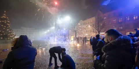 Folk ser på fyrverkerier olagligt på en stadsgata med julgran och byggnader.