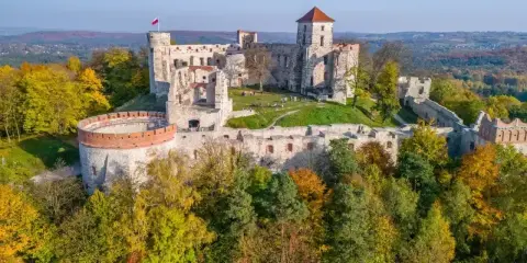 Ruiny zamków Jury Krakowsko-Częstochowskiej na tle jesiennych lasów. Majestatyczne kamienne mury i wieże, polska flaga powiewa na wietrze.
