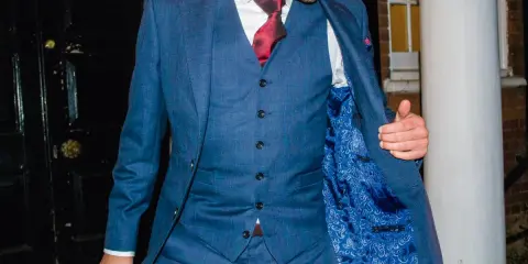 A man in a blue checkered suit, white shirt, and red tie. He's showing off the paisley lining of his jacket, and the bottom button on his vest is unbuttoned.