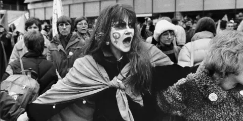 En kvinna med ansiktsmålning och symbolen för kvinnor ropar under en demonstration för sveriges demokratisering.