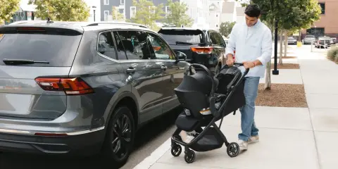 Hombre empuja un cochecito con un sistema sujeción infantil silla coche, junto a un coche gris.