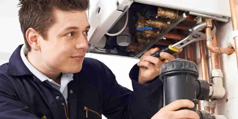 Instalator pracuje przy kotle, dokręcając rury kluczem. Może sprawdzać, czy jest tam inhibitor, który chroni system przed korozją.