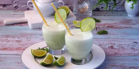 Dwa orzeźwiające drinki z mlekiem skondensowanym, ozdobione plasterkami limonki i miętą, na talerzu.