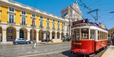 Röd spårvagn i Lissabon, perfekt för en resa med interrail europa. Gula byggnader och en solig dag.