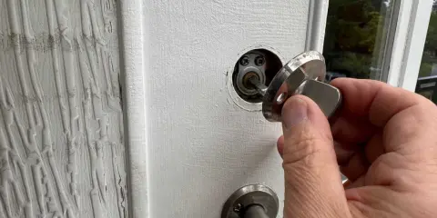 En hand håller en nyckel till en vit dörr, redo att aktivera den smarta låsmodulen.