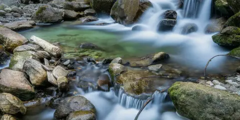 Acqua cristallina scorre tra rocce muschiose, creando un effetto seta su un ruscello di montagna.