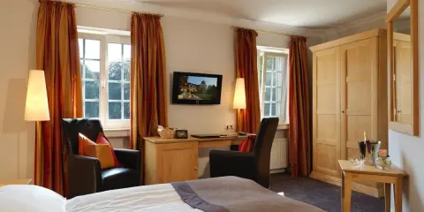 Gemütliches Zimmer mit Blick auf die Klosterpforte Harsewinkel. Einladende Sessel, Schreibtisch und ein großes Bett.