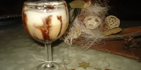Pyszny drink z adwokatem, udekorowany czekoladą, na tle świątecznych ozdób.
