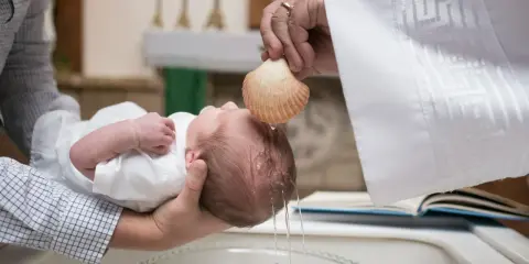 Chrzest dziecka. Kapłan polewa główkę niemowlęcia wodą święconą z muszli. To ważny moment, jak ile daje się na chrzciny.