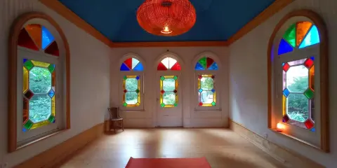 Un tapis de yoga orange attend dans une pièce lumineuse aux vitraux colorés, créant une atmosphère de maison bienveillante.