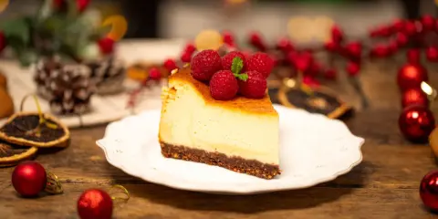 Sernik creme brulee z malinami i miętą, udekorowany na drewnianym stole, w świątecznej scenerii.