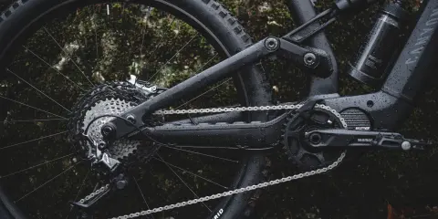 Część roweru elektrycznego z napędem **Shimano EP8** w deszczu. Widoczna kaseta, przerzutka, łańcuch i korba.