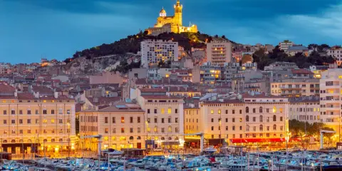 Il porto di Marsiglia MSC, con le luci della città e la basilica di Notre-Dame de la Garde in cima alla collina, crea uno scenario suggestivo al crepuscolo.