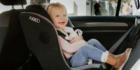 Uśmiechnięta dziewczynka w foteliku rwf, przytulająca pluszową zabawkę, bezpiecznie podróżuje samochodem.