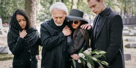 Smutna rodzina w czarnych strojach, zastanawiająca się, jak się ubrać na pogrzeb znajomego. Trzymają kwiaty.
