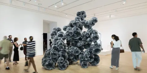 Visitors admire a large, dark, spherical sculpture in a bright gallery space, typical of Indianapolis Museum of Art photos.