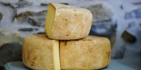 Formaggio Fossa stagionato, con crosta rustica e pasta gialla, impilato su uno sfondo di pietra grezza.