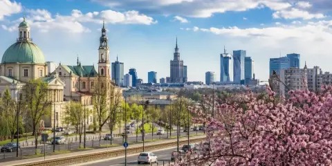 Majówka w Warszawie: zabytkowy kościół i nowoczesne wieżowce na tle kwitnącej wiśni.