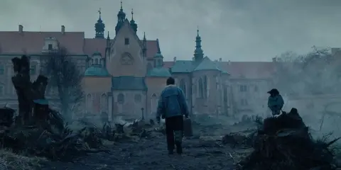 Mężczyzna z walizką idzie w stronę zamku, na pierwszym planie kruk na pniu.