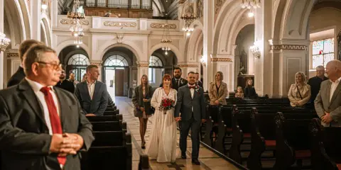 Para młoda idzie do ołtarza przy akompaniamencie piosenki na wejście. W kościele zgromadzeni goście.
