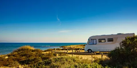 Un camper bianco sosta su un sentiero sabbioso con vista sul mare blu intenso. Un'avventura indimenticabile in camper all'Isola d'Elba.