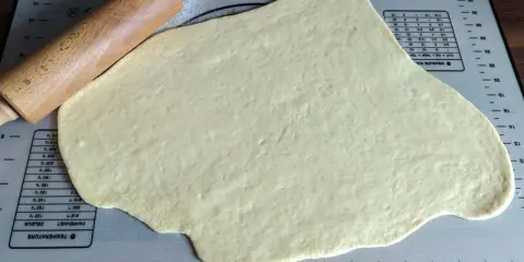 Pâte à beignet légère et croustillante étalée sur un tapis de pâtisserie avec un rouleau à pâtisserie en bois.