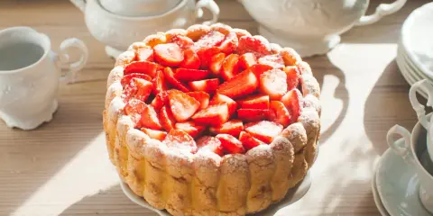 Gâteau frais garni de fraises, entouré de biscuits cuillère et saupoudré de sucre glace. Une belle table de thé.