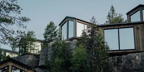 Moderna trähus med stora fönster klättrar uppför en stenig sluttning, omgivna av tallar. En idyllisk camping Lapland resort.