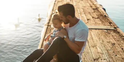 Ojciec tuli córkę na drewnianym pomoście nad wodą.