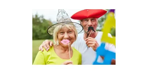 Uśmiechnięci seniorzy w zabawnych nakryciach głowy i rekwizytach, jak na wieczorki zapoznawcze dla seniorów.