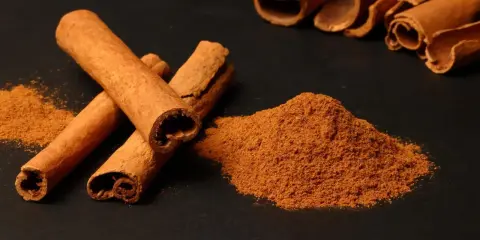 Kora cynamonu i mielony cynamon na czarnym tle. Zastanawiasz się, ile cynamonu dziennie jest bezpieczne?