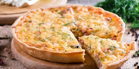 Pyszna tarta z porem i boczkiem, posypana serem i koperkiem, z kawałkiem już wyjętym.