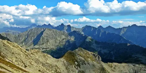 Widok na skaliste pasmo górskie, gdzie każdy zawrat szczyt zapiera dech. Błękitne niebo z białymi chmurami nad ostrymi grzbietami.