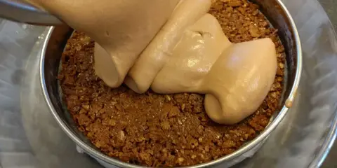 Une crème onctueuse est versée sur une base croustillante chocolat dans un moule.