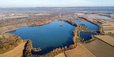 Widok z lotu ptaka na zbiornik wodny otoczony jesiennymi drzewami i polami kukurydzy. To idealne miejsce na próbę wędkarską.