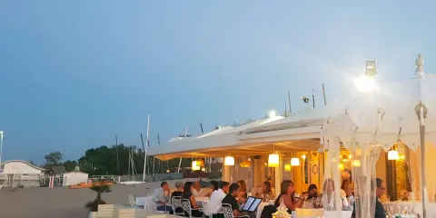 Serata in uno dei ristoranti della Riviera Romagnola, con tavoli apparecchiati sulla sabbia e luci soffuse.